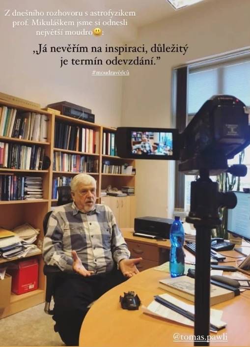 starszy mężczyzna siedzący przy stole, z tyłu regały z książkami