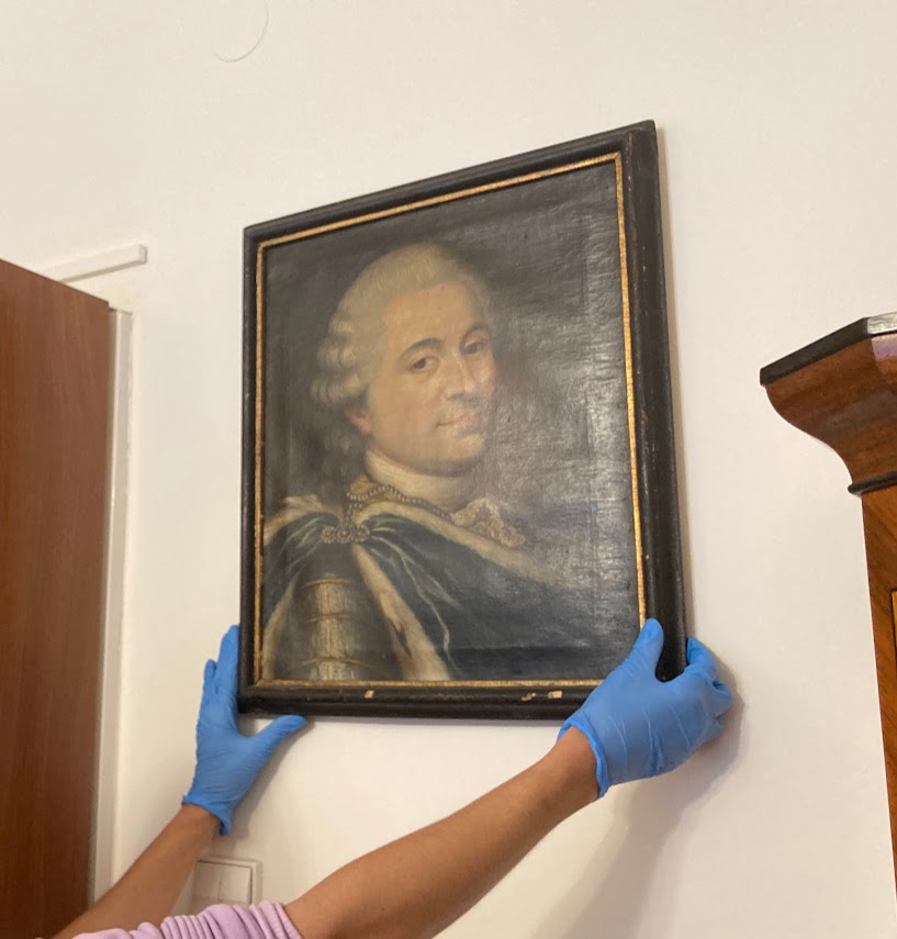 Obraz Króla w trakcie zdejmowania ze ściany; widoczne rękawiczki eksperta