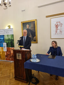 Jedna osoba stoi za mównicą, druga siedzi przy stole