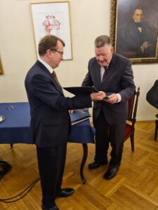 Dwie osoby stoją, jedna trzyma twardą teczkę z życzeniami